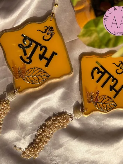 A pair of bright yellow resin Shubh Labh hangings with elegant pearl tassels. These are perfect for adorning the entrance of your home during Diwali and other festivals.