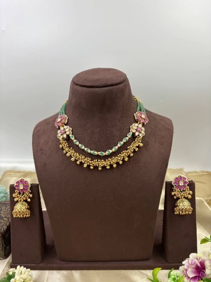 The Rishika premium antique gold set. It features a unique double-layer design with one layer of golden beads and another of green beads, adorned with floral motifs in pink stones.