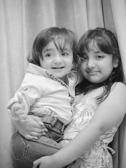 A classic black and white portrait of a big sister holding her little brother, a timeless keepsake of their bond.