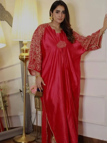 A vibrant red kaftan with gold embroidered sleeves. This comfortable yet glamorous piece is perfect for a festive evening at home or a relaxed celebration with friends.