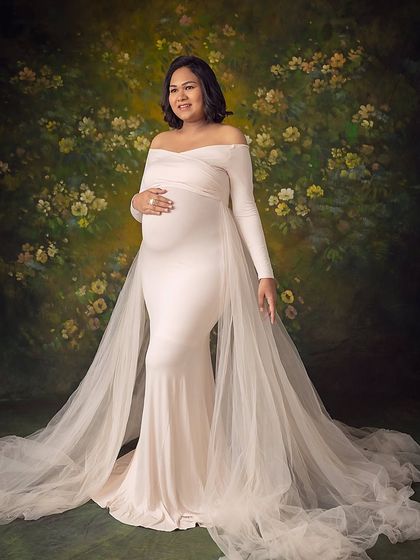 A confident and radiant pose. The full-length view shows off the elegant maternity gown with its sheer, flowing train.