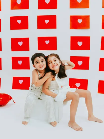 A sweet hug and a shared smile. The simple red heart background adds a pop of color and love to this sibling photoshoot.