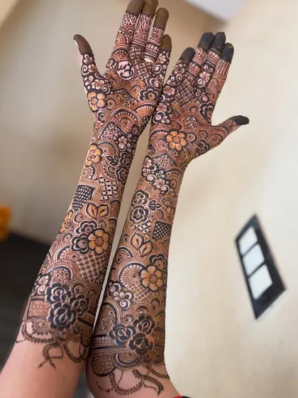 A stunning floral henna design that covers the back of the hands and arms. The mix of bold flowers and delicate checkered patterns is a classic Indo-Arabic style.