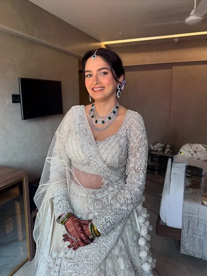 Ivory dreams and timeless elegance. This bride looks absolutely serene and beautiful for her reception in a stunning white lehenga. The makeup is soft, with a pop of color from the floral bun.