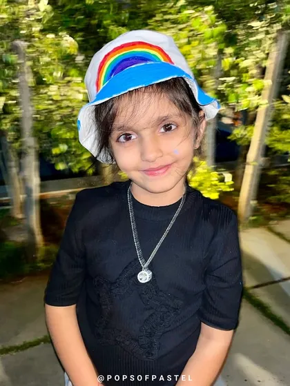 A little girl proudly models the rainbow bucket hat she painted herself at a birthday party.