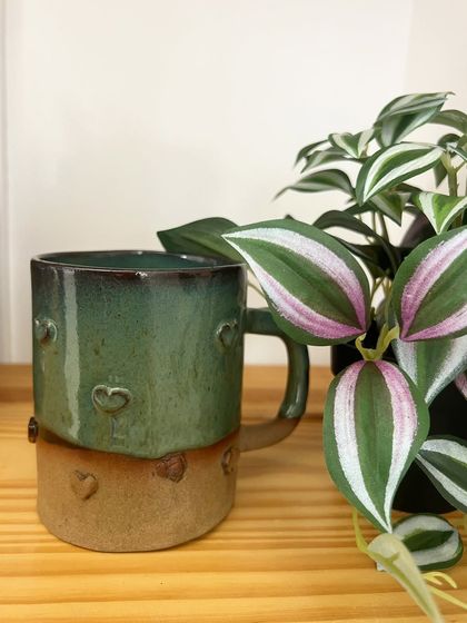 A sweet, heart-stamped mug with a lovely green glaze. This piece is perfect for gifting to a loved one or for adding a touch of warmth to your own mug collection.