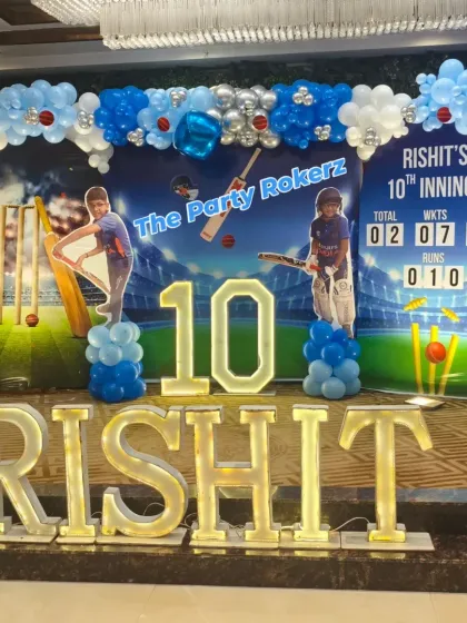 A grand cricket theme decoration for a 10th birthday party. We designed a stadium-style backdrop, complete with a scoreboard and custom cutouts, framed by a blue and white balloon arch and large marquee letters for the name.