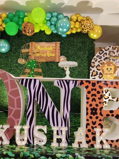 A full stage setup for a jungle-themed first birthday. This decor features large 'ONE' letters with animal prints, a green wall backdrop, and character cutouts.