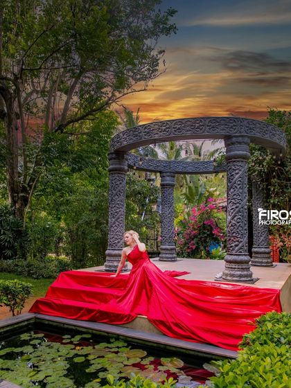 A wide shot of the model in the red dress at our stone gazebo, showcasing the beautiful contrast with the green surroundings.