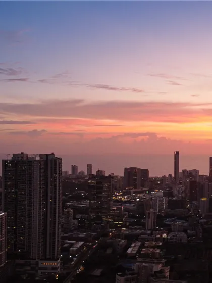 A close-up view of Mumbai's coastal buildings at dusk, with the sky showing soft hues of pink and orange after sunset.