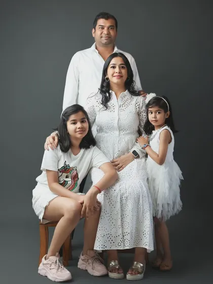 This is a classic family portrait from our Noida studio. We arranged this family of four, with parents and two daughters, for a timeless look against a simple grey backdrop, highlighting their connection and coordinated white outfits.