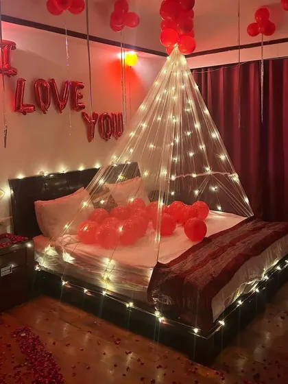 An intimate room setup with an "I Love You" theme, featuring a fairy light canopy over the bed and red balloons.
