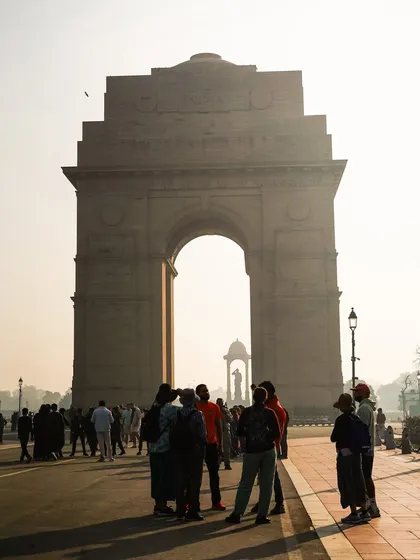 A guide shares stories with a group in the golden morning light at India Gate. Our tours are designed to bring the history of such iconic monuments to life.