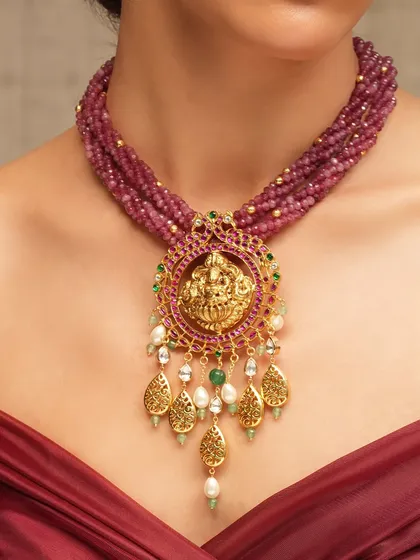 A magnificent temple jewelry piece, featuring a large pendant with a deity motif, strung on a multi-strand ruby bead necklace.