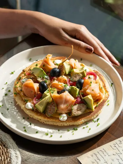 A savory pancake topped with smoked salmon and avocado. This shot showcases a unique and upscale brunch offering.