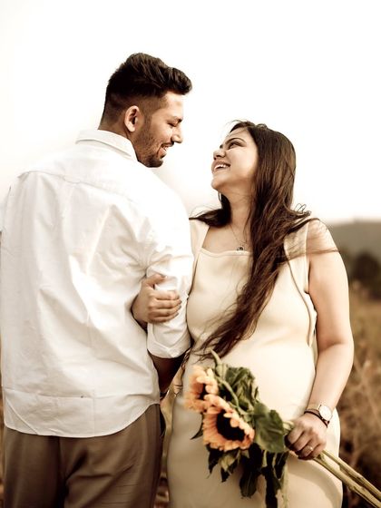 A romantic portrait of the couple in a golden field, looking at each other with love. The sunflowers she holds add to the warm, happy feeling.