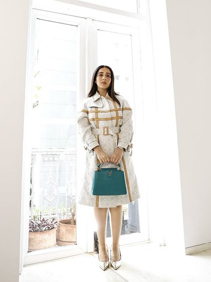 A full shot showcasing the iconic Louis Vuitton coat and bag. The makeup is clean and minimal, ensuring it enhances the model's features without distracting from the luxury products.
