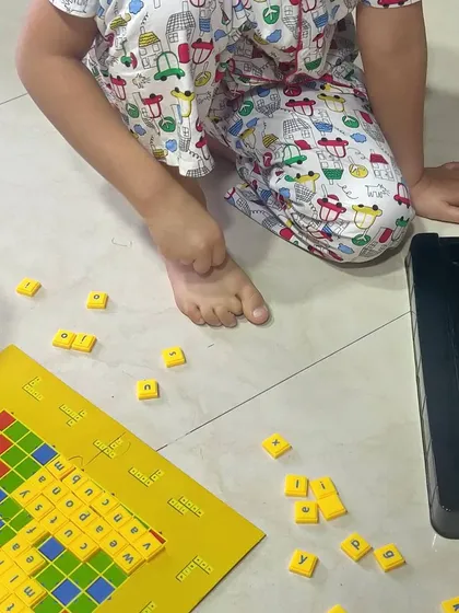 We make learning words a game, not a chore. Using a simple Scrabble board, we practice spelling and reading three and four letter words. It’s a playful way to build vocabulary and early literacy skills right on the living room floor.