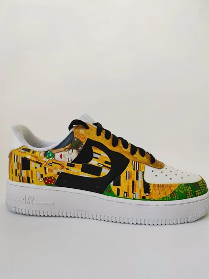 A side profile of "The Kiss" AF1. The contrast between the white shoe, the black swoosh, and the golden artwork is stunning.