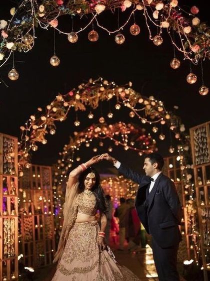 A magical wedding entrance tunnel. The archway is decorated with flowers and countless hanging glass globes with candles, creating an enchanting path for the couple and guests.