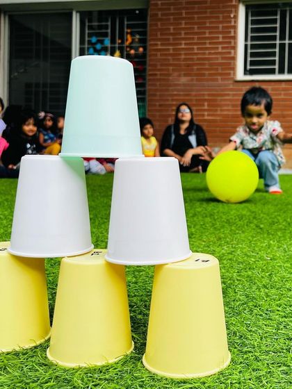 This cup stacking and knock-down game is a simple yet effective activity for toddlers. It helps develop their hand-eye coordination and understanding of cause and effect while they aim the ball.