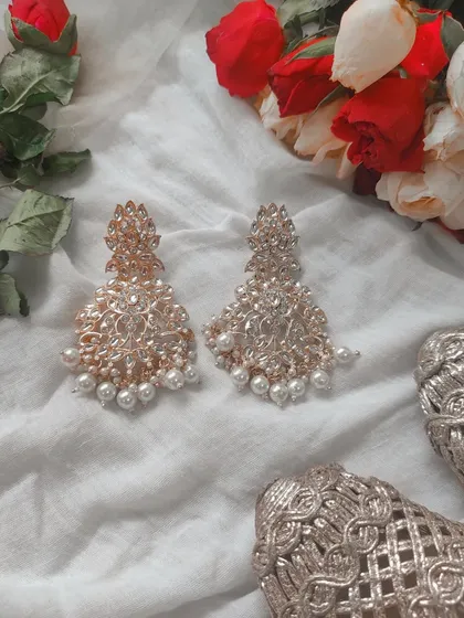 A clean and simple flat lay of ornate pearl earrings next to a bouquet of roses, perfect for bridal or special occasion jewelry.