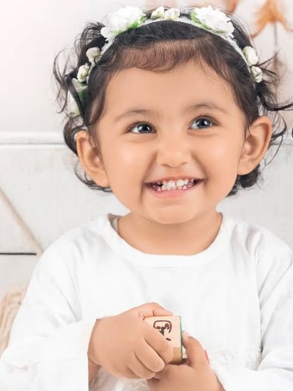 A beautiful, happy portrait of a little girl with a flower headband against a simple white background.