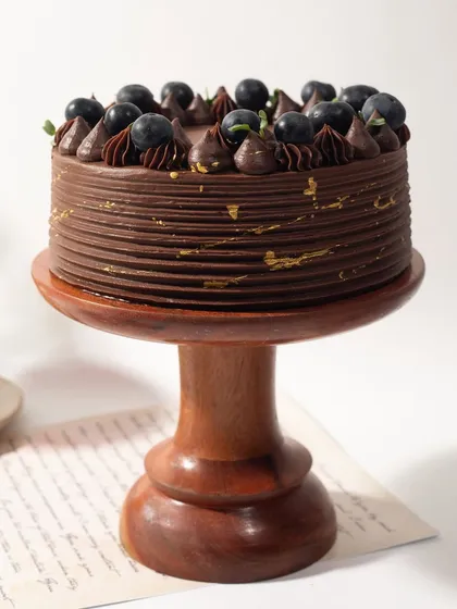 My Winter Berry Cake is a classic. The rich chocolate cake is complemented by fresh, juicy blueberries and delicate piping, all resting on a rustic wooden stand.