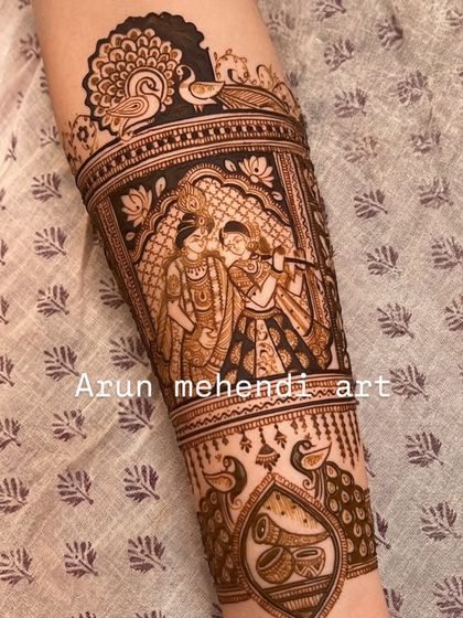 A detailed forearm piece showing Radha and Krishna playing the flute, surrounded by peacocks. A beautiful symbol of divine love.