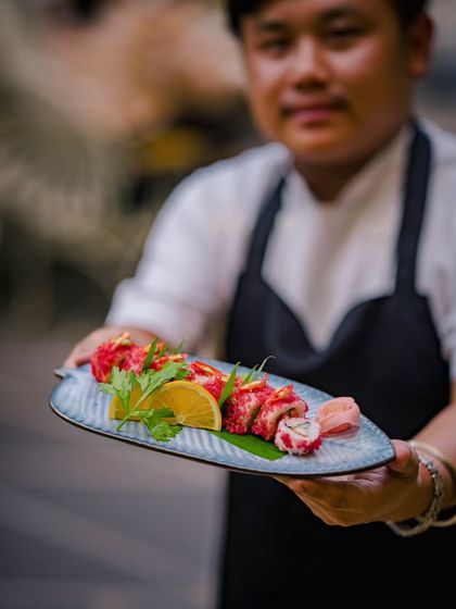 A chef presents the Kyoto Ember Uramaki, its vibrant red tobiko and fresh garnish making it a feast for the eyes.