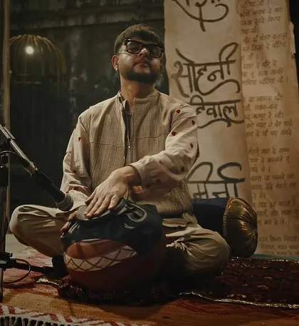 A shot of a musician from the 'Ishqbawla' set. The lighting is intimate and focused, using a single key light to highlight the artist and his instrument against a dark, textured background.