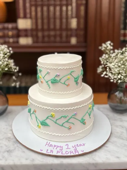 A sweet and simple two-tier cake with hand-piped floral vines. This design is perfect for an anniversary or an intimate celebration, offering a touch of whimsy and charm.