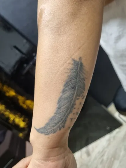 The original faded feather tattoo on the forearm before the cover-up process began.