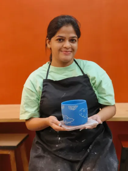 A student proudly displays her finished sgraffito pot, featuring a charming cloud pattern carved into a vibrant blue surface. The contrast created by this technique is striking.