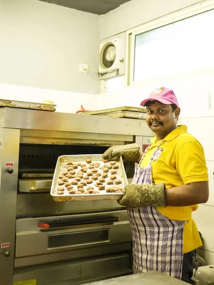 Baking happiness is a team effort. A smiling chef holds a tray of freshly baked treats, showcasing the love and care we put into our work.