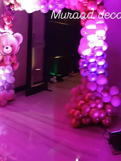 An entrance arch for a teddy bear themed party. The arch is made of pink and metallic balloons, with a teddy bear foil balloon integrated into the design to welcome guests.