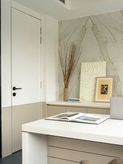 A close-up of the CEO's desk, showing the fine details of the two-tone door, the book-matched marble, and the curated art pieces.
