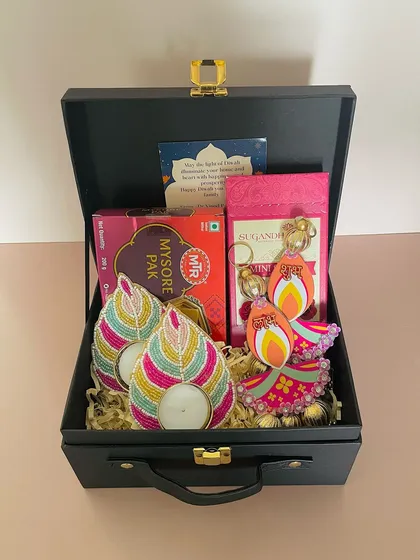This black suitcase hamper combines traditional and modern elements. It features colorful beaded T-light holders, Mysore Pak, and a keychain, all beautifully arranged for a memorable Diwali gift.