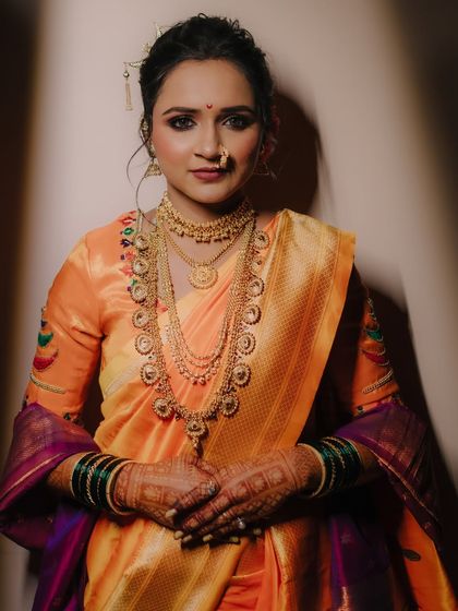 A direct, beautifully lit portrait showing the bride's complete look, from her makeup and hair to her layered necklaces and vibrant saree.