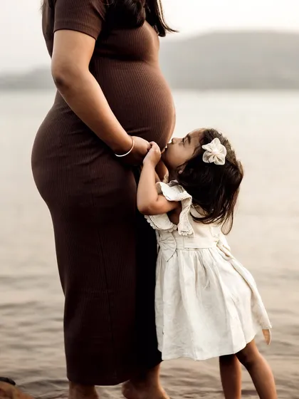 An incredibly tender moment between a mother and daughter by the water. The little girl gives her mom's baby bump a sweet kiss, a beautiful display of sibling love before they've even met.