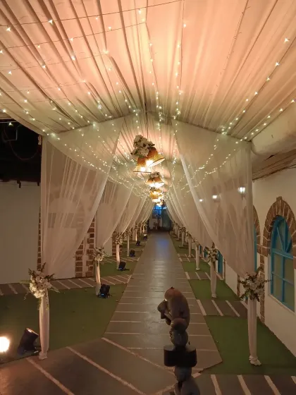 A beautiful, long walkway decorated with a canopy of draped fabric and fairy lights. The path is lined with floral arrangements, creating an elegant and dreamy entrance for a resort wedding.