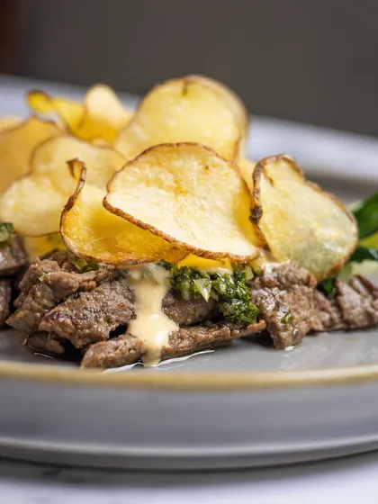 A close-up of the char-grilled steak in our Steak and Frites, topped with béarnaise and paper-thin truffle potato crisps.
