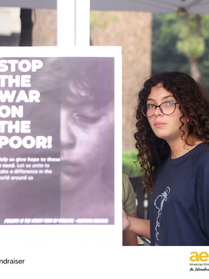 A student stands by a poster she created to raise awareness about poverty. Our service learning projects encourage students to use their voices and creative skills to advocate for issues they care about.