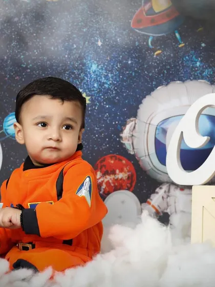 A pensive moment for our little astronaut before his first space mission. This shot from a space-themed first birthday session highlights the detailed astronaut suit and the dreamy, cloud-like floor.