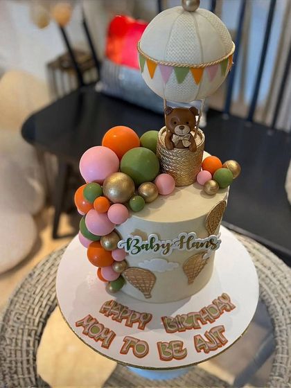 A closer look at the "Baby Hans" cake, showing the adorable teddy bear in the hot air balloon basket and the colorful balloon cascade.