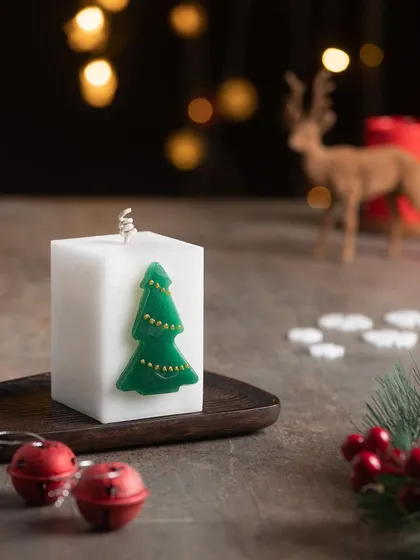 This white square pillar candle is decorated with a simple green wax Christmas tree. It's modern and festive.