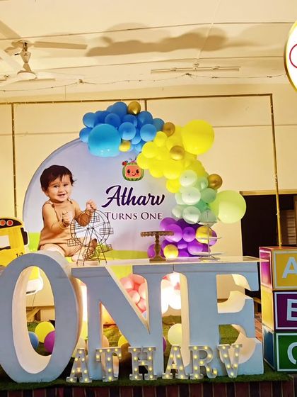 A Cocomelon-themed first birthday with a large 'ONE' table. The setup includes character cutouts, a themed backdrop, and a 'ATHARV' marquee.