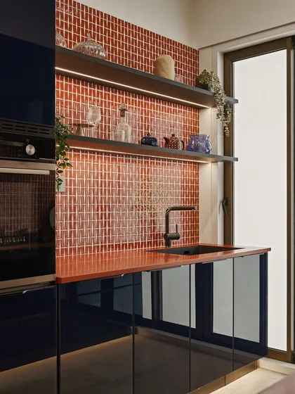 For this show apartment kitchen, we chose a fun and lively color combination of dark blue cabinets and a deep orange countertop. The backsplash is made of glossy red subway tiles, adding texture and vibrancy.