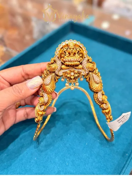 This stunning bajuband is fully studded with sparkling stones around a central Lakshmi motif. The peacock designs on the side add to its grandeur, making it a perfect rental piece for a royal bridal look.