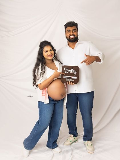 A cute announcement shot with a "Baby Loading" sign. The couple's casual white shirts and jeans create a relaxed and modern vibe.